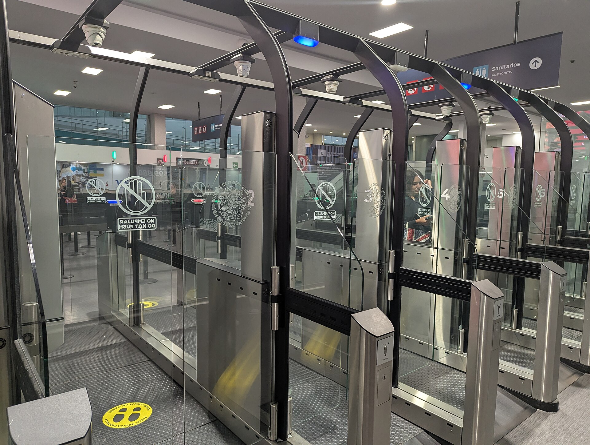 A row of glass automated immigration gates with Mexican government emblems in the arrivals hall of Terminal 1 at Mexico City airport