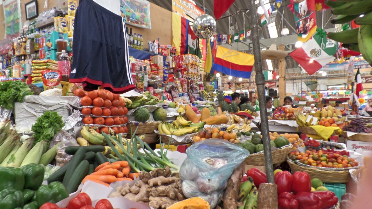 A produce stall piled with tomatoes, bananas, chillies, corn and ginger inside the Mercado Medellin in Colonia Roma, with Latin American flags hanging from the roof
