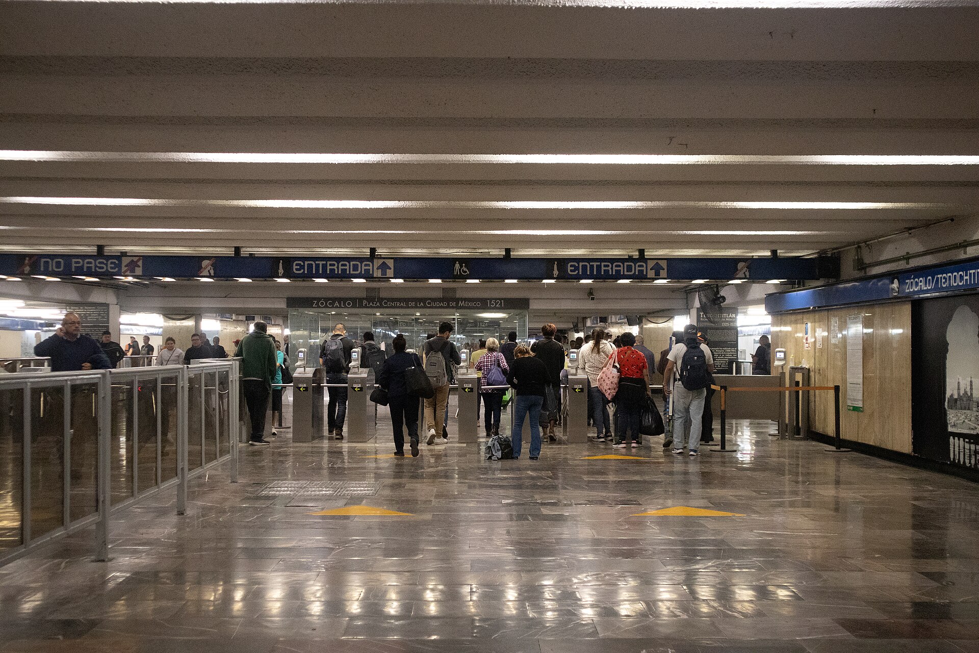 Passengers passing through the turnstiles at Zócalo Tenochtitlan Metro station in Mexico City beneath signs reading Entrada