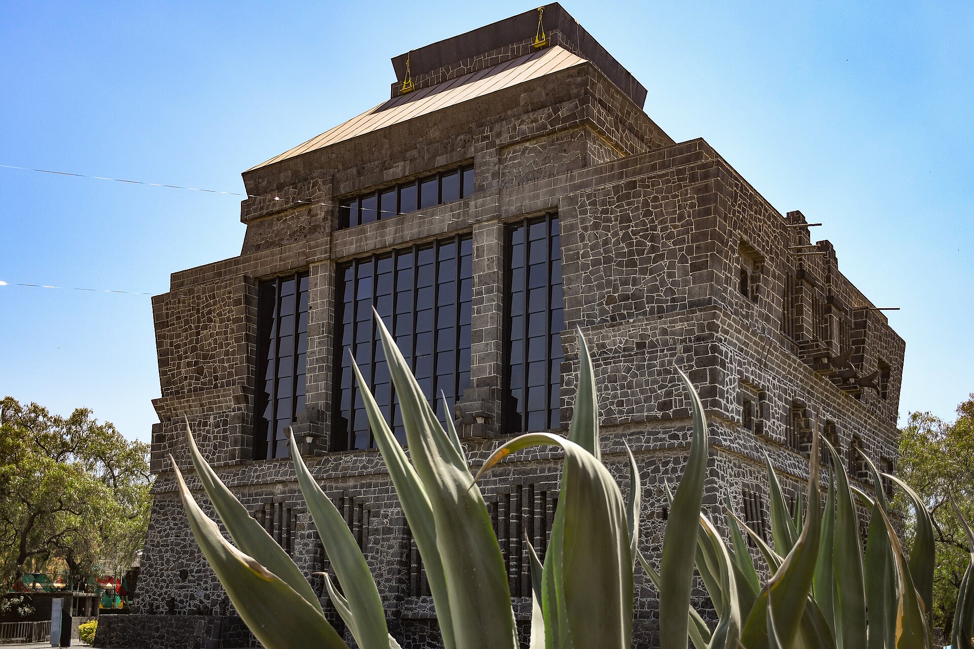 The dark volcanic stone façade of the Museo Diego Rivera-Anahuacalli in Mexico City, a stepped pyramid-like building, with agave plants in the foreground