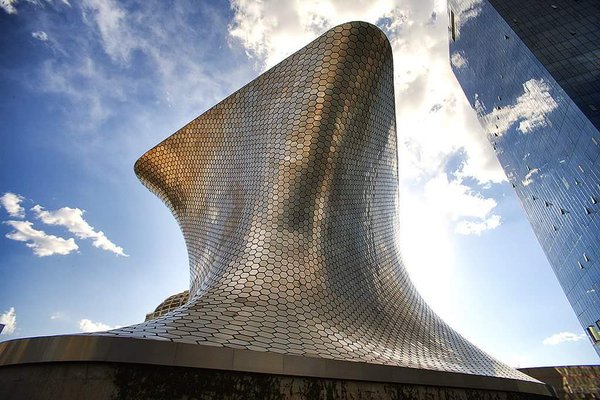 The curving silver hexagon-tiled exterior of the Museo Soumaya in Mexico City seen from below against a blue sky