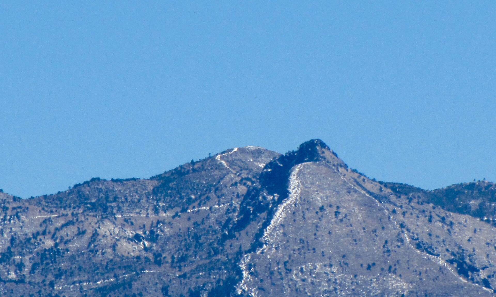The rocky, lightly snow-dusted summit ridge of Pico del Águila on the Ajusco, with trails visible traversing the slopes beneath a clear blue sky