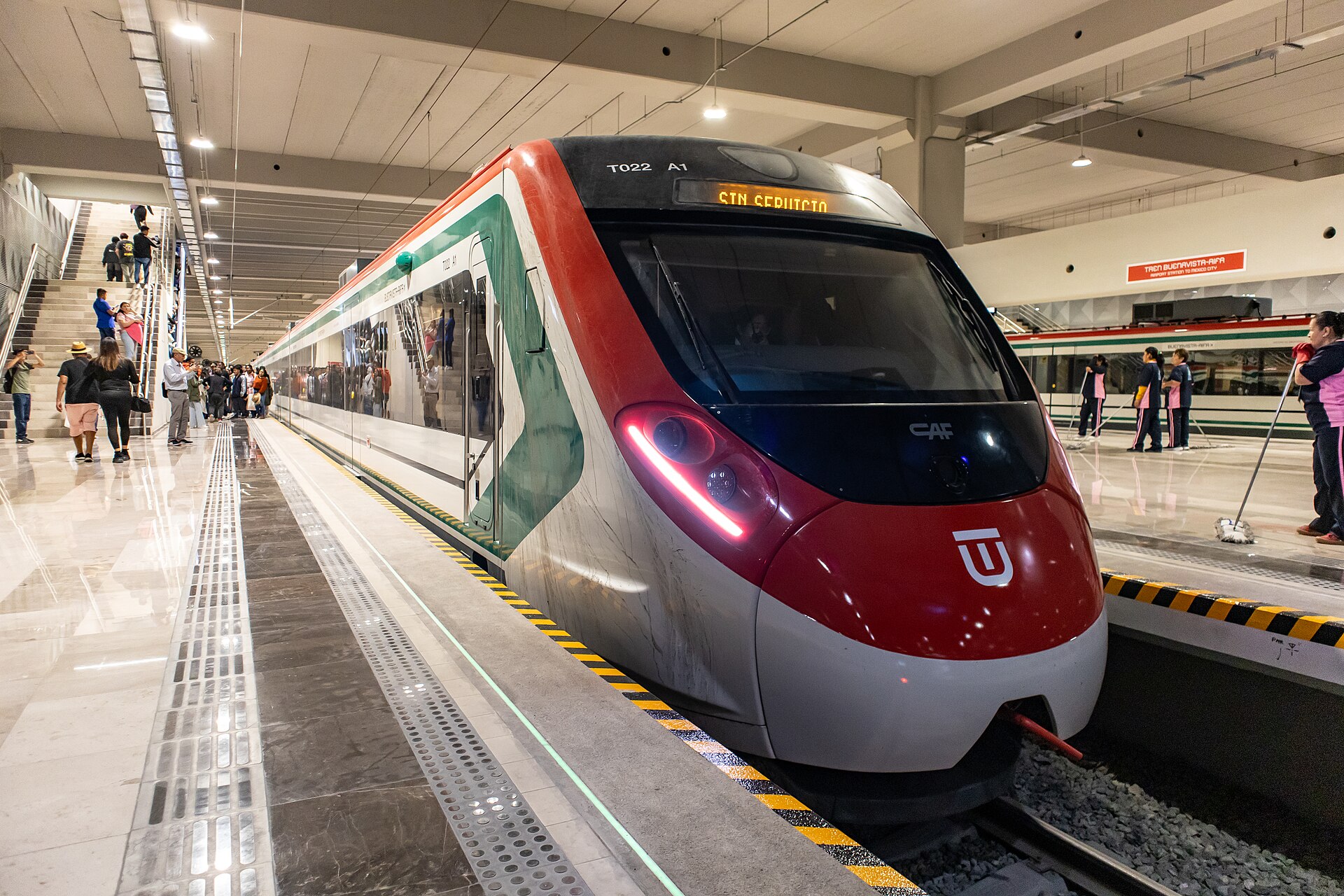 A red, white and green suburban train standing at a platform inside AIFA station, with signage reading Tren Buenavista-AIFA Airport Station to Mexico City