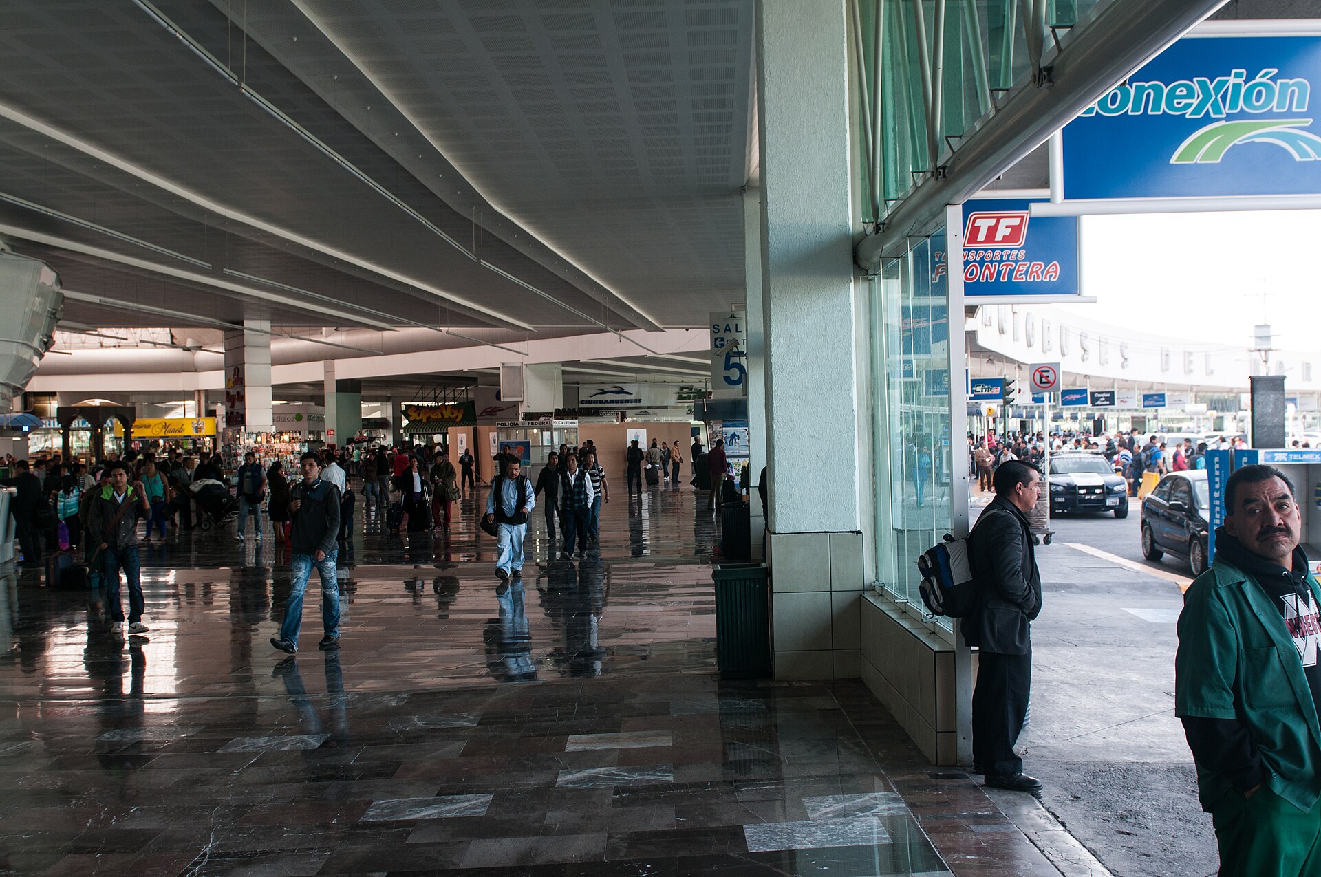 The long covered concourse of the Terminal del Norte in Mexico City, with a polished stone floor, passengers walking past shops and a hanging sign for Sala 5